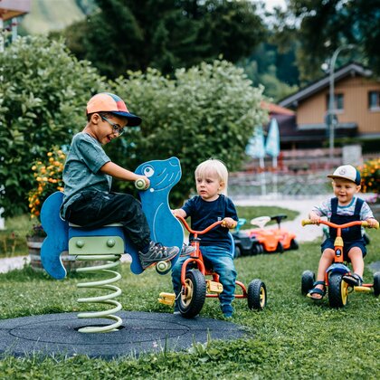 Kind auf Wipptier und Kinder auf Tretrollern